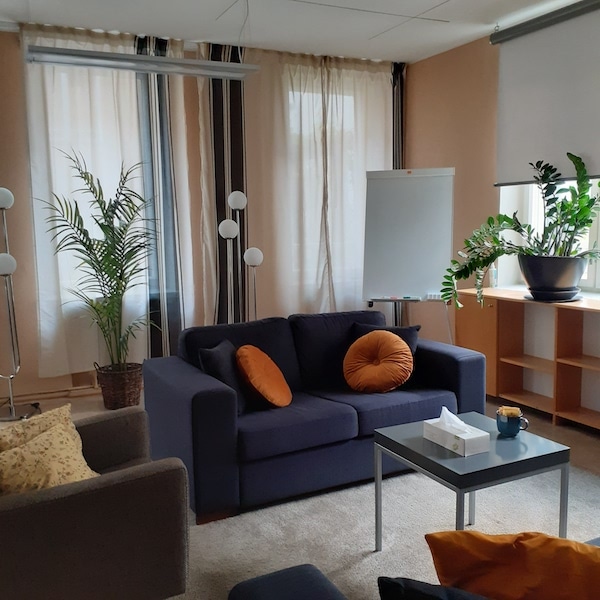 Kuvassa näkyy Kampin terapiatilan huone, jossa on sohva, nojatuoli, pieni pöytä ja kasveja.